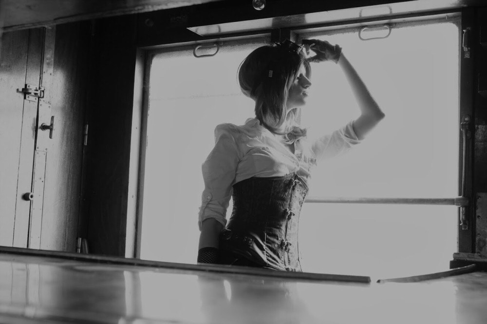 femme gothique en costume steampunk et cheveux longs en contrejour dans l'encart d'une fenêtre