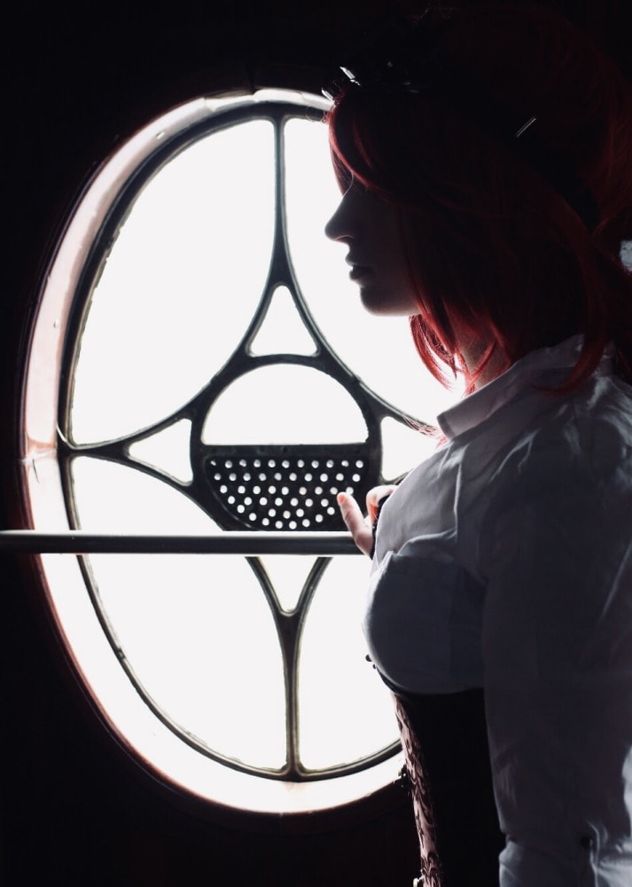femme gothique en costume steampunk et cheveux longs portrait de profil en contrejour rouge devant une rosace