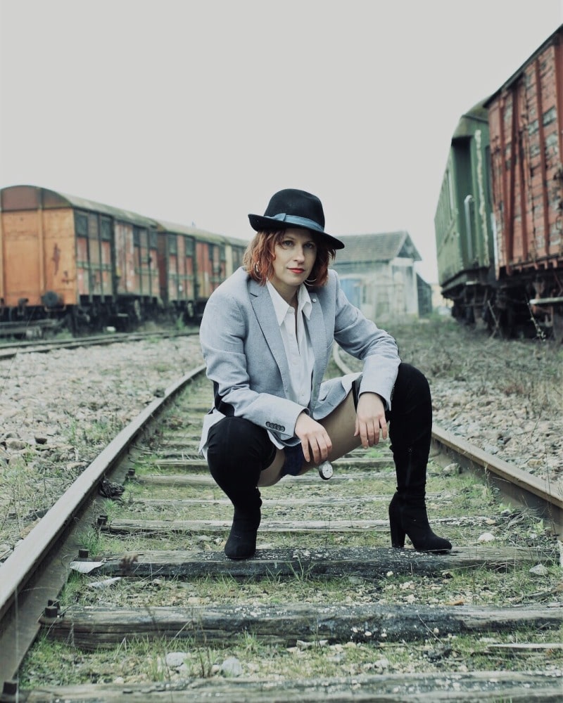 femme en tenue d'homme sur des rails devant de vieux trains