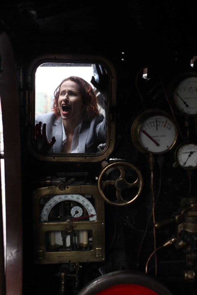 femme en tenue d'homme criant devant une ancienne locomotive
