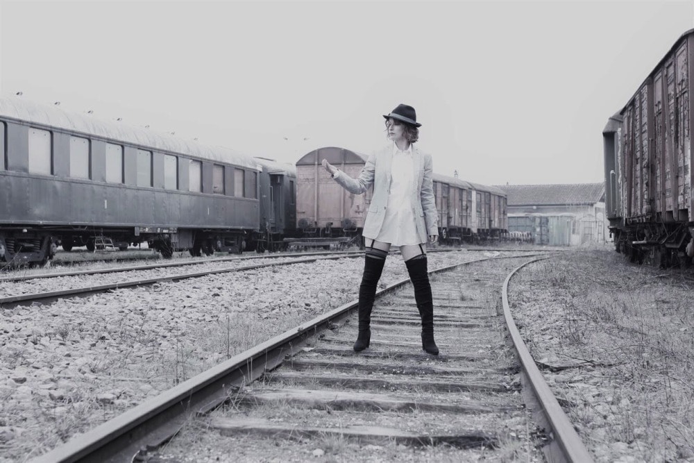 femme en tenue d'homme sur des rails devant de vieux wagons