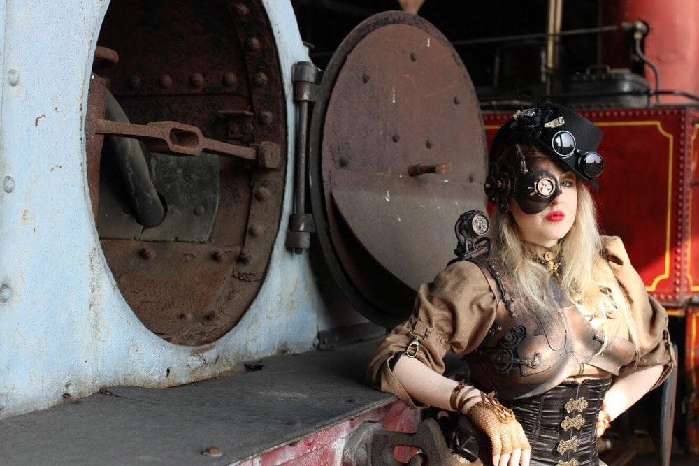 femme en costume steampunk devant une chaudière de locomotive ouverte