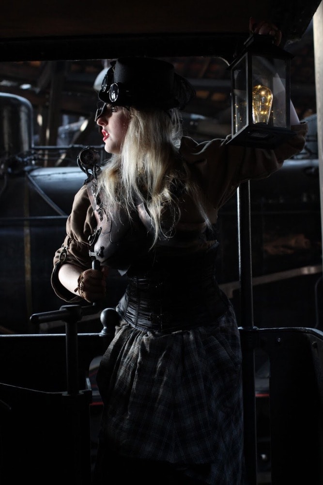 femme en costume steampunk devant une ancienne locomotive regardant à gauche