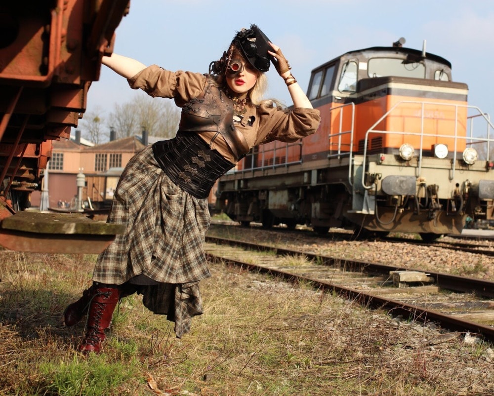 femme en costume steampunk devant un rail de voie ferrée abandonnée