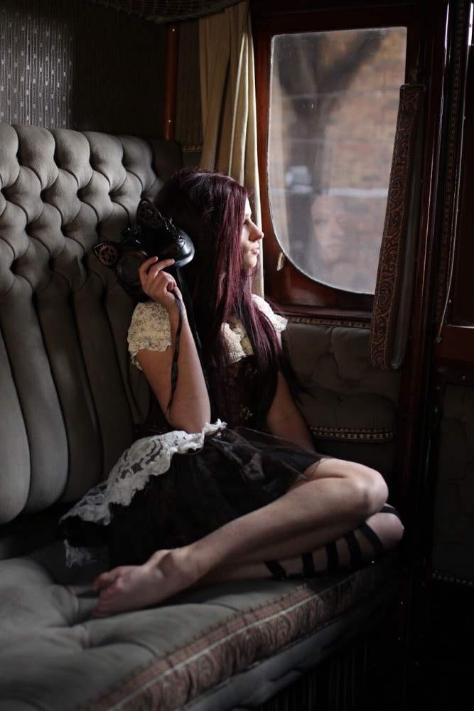 femme gothique en costume steampunk et cheveux longs assise dans un wagon ancien de luxe regardant par la fenêtre