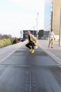 Homme habillé en jaune avec chaussures à talons accroupies sur les grilles de l'escalier de la BNF