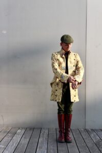 Homme lifestyle en manteau long jaune et casquette debout devant un mur