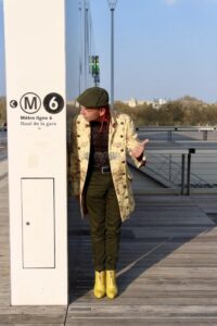 Homme en manteau long jaune et casquette faisant du stop à côté d'un mur