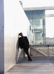 Homme lifestyle en costume vert et bottes rouges penché sur un mur du parvis de la BNF