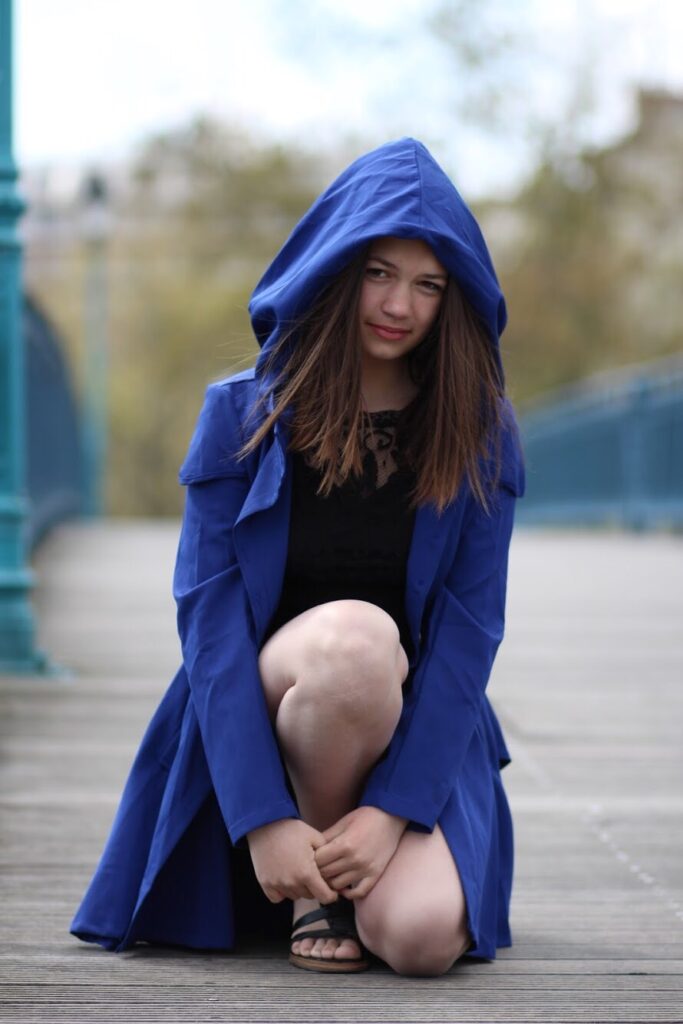 Shooting modele adolescente jeune fille photo-thérapeutique avec Morgane 13 ans en extérieur portant une cape à capuche bleue assise sur un pont robe dentelle noire