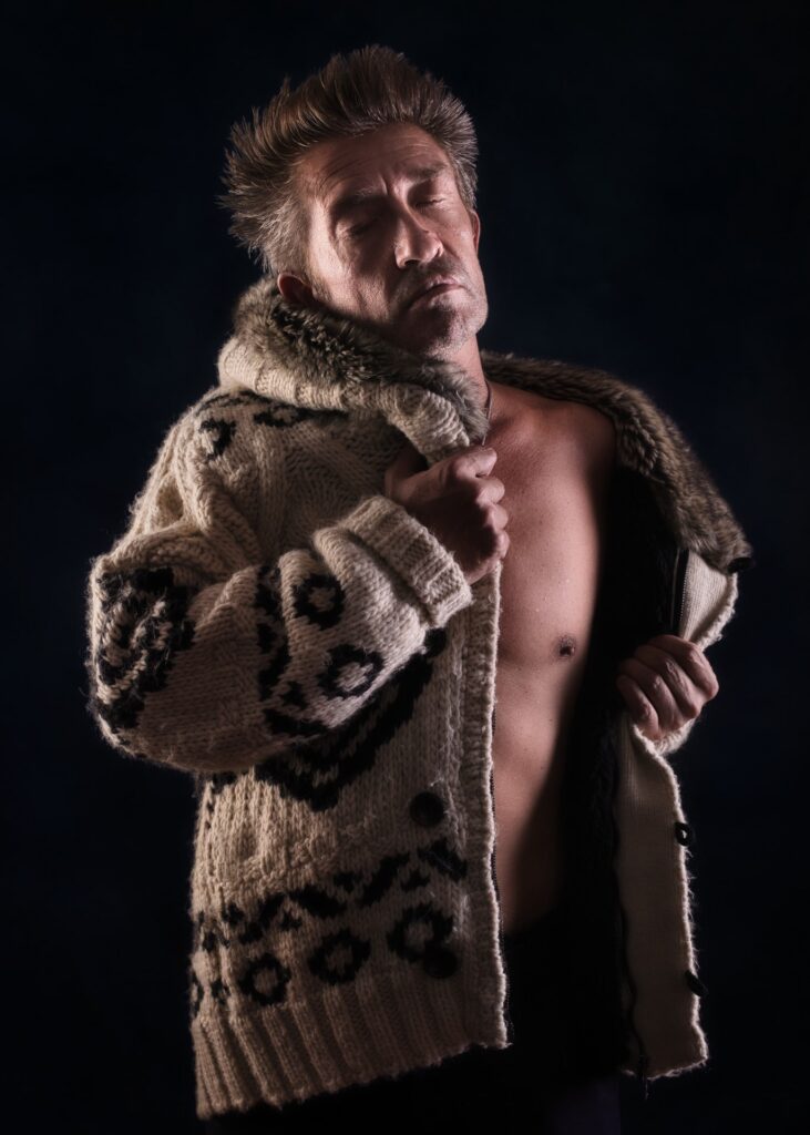 modèle photo homme en nu artistique clair obscur dans un manteau en laine et fourrure fermant les yeux