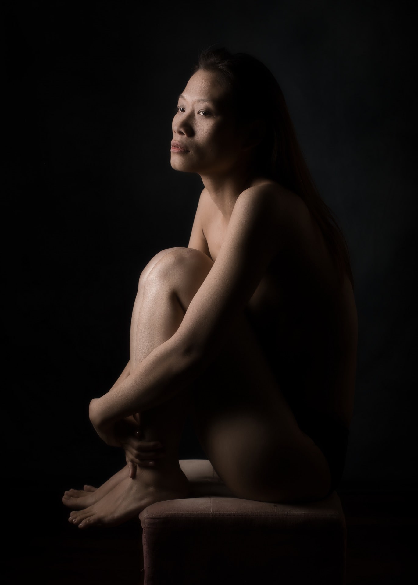 Femme asiatique de profil assise sur un tabouret en nu artistique et clair obscur