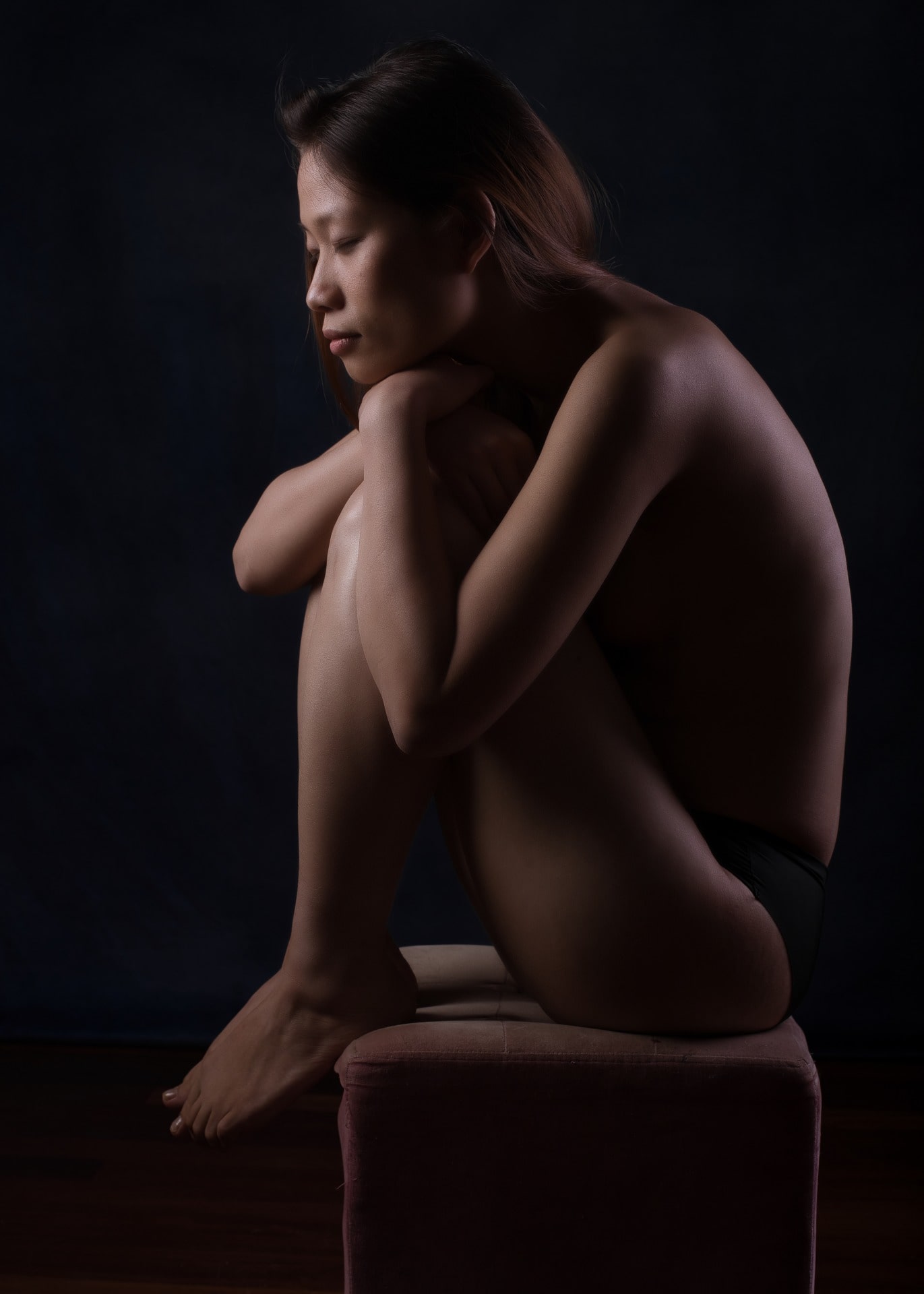 Femme en nu artistique et clair obscur assise sur un tabouret de profil