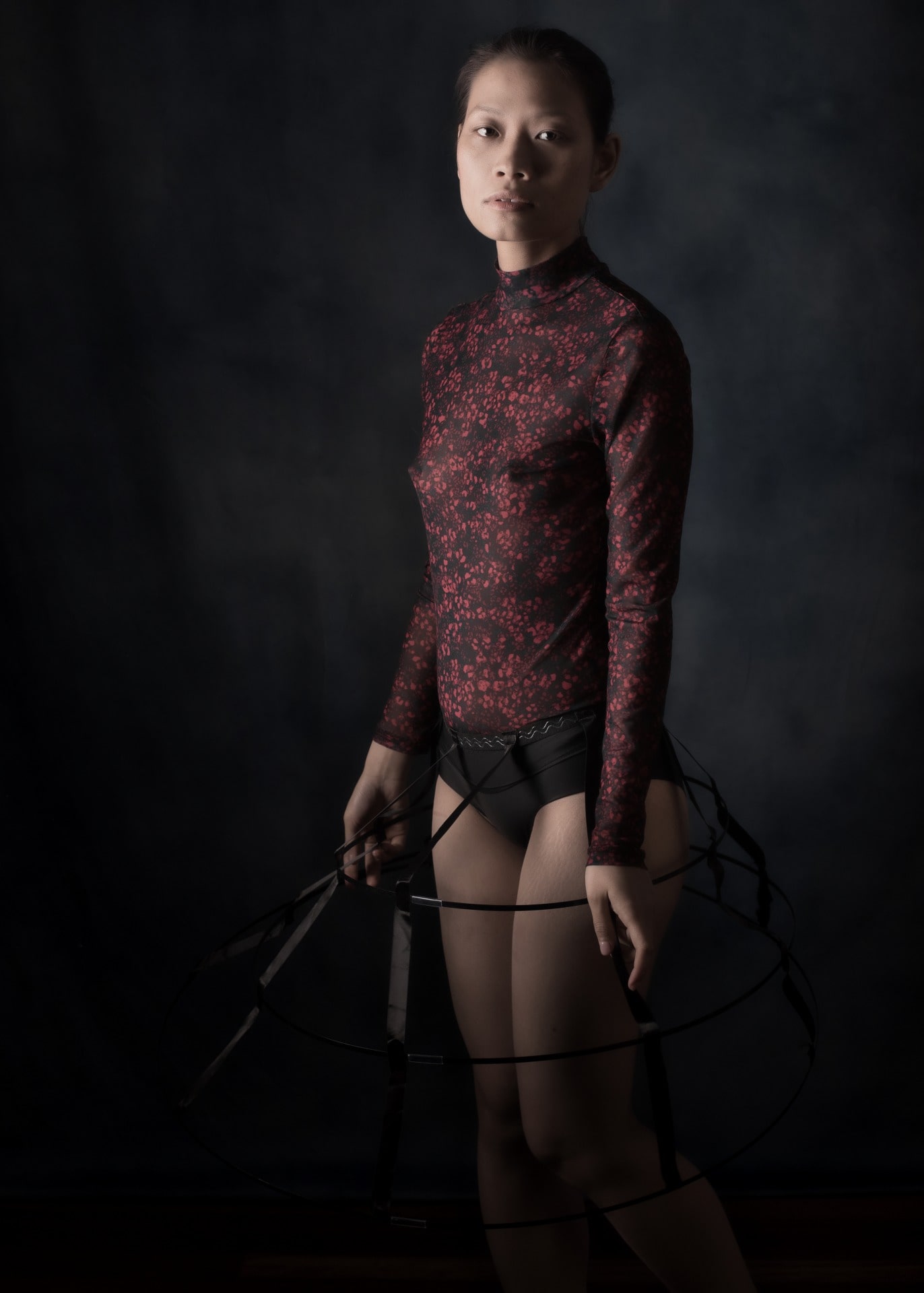 Femme asiatique debout en body rouge et crinoline l'air enfantin en clair obscur