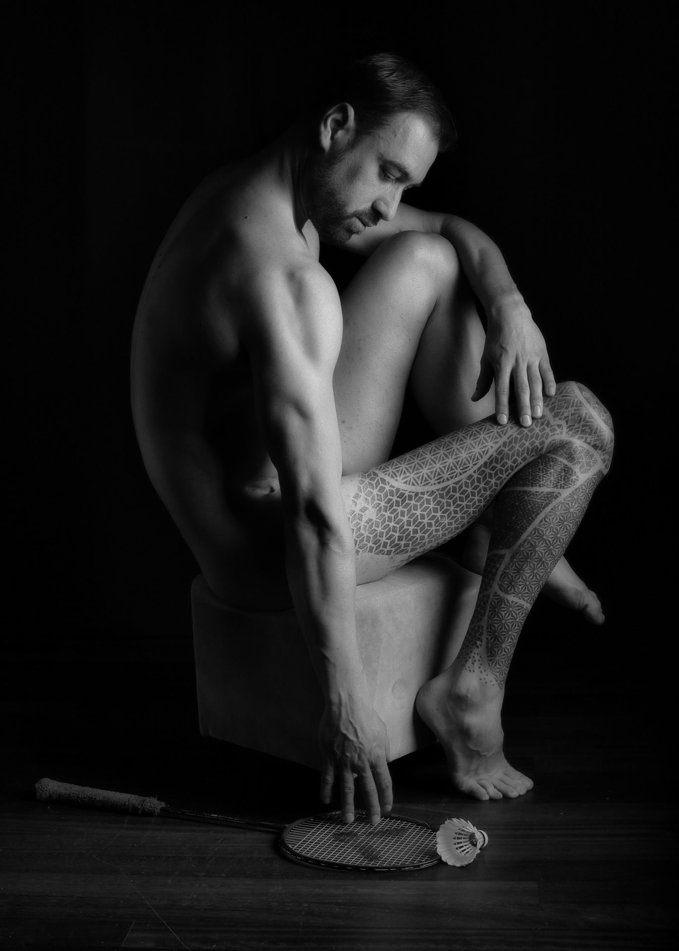 homme en nu artistique tatoué assis sur un tabouret une jambe tatouée atrophiée 