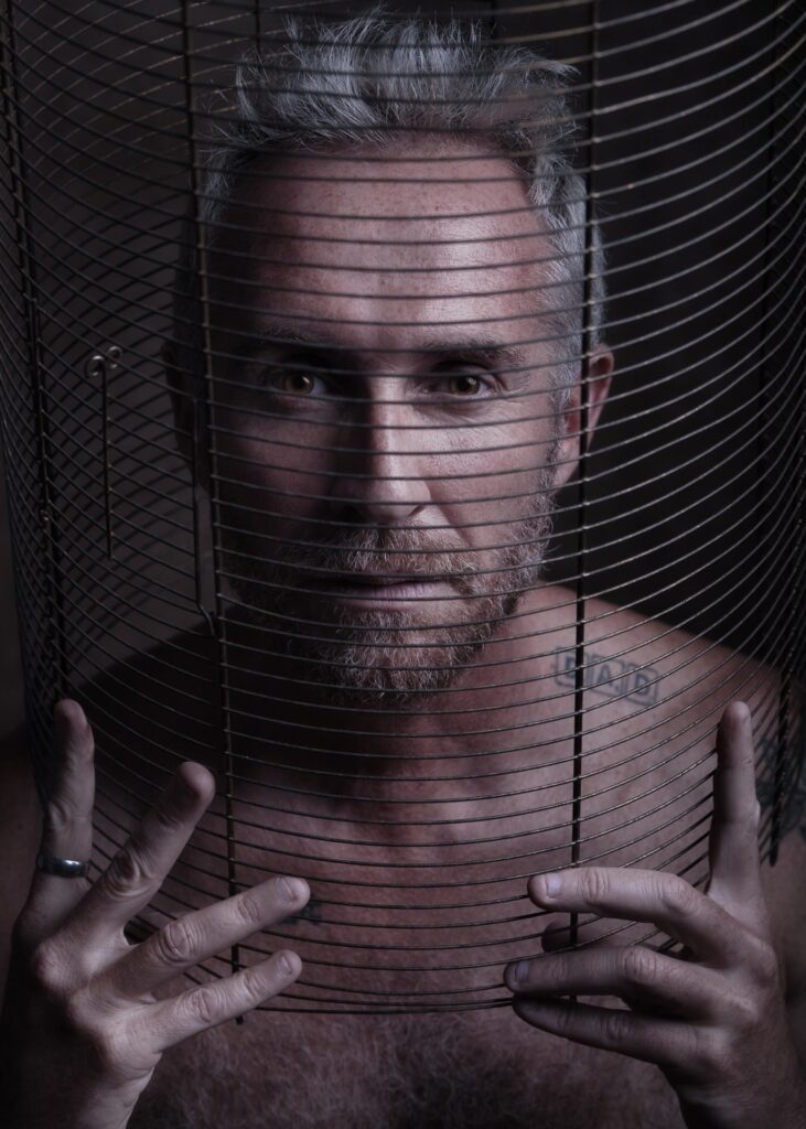 portrait homme nu en cage cheveux blanc et barbu tatoué