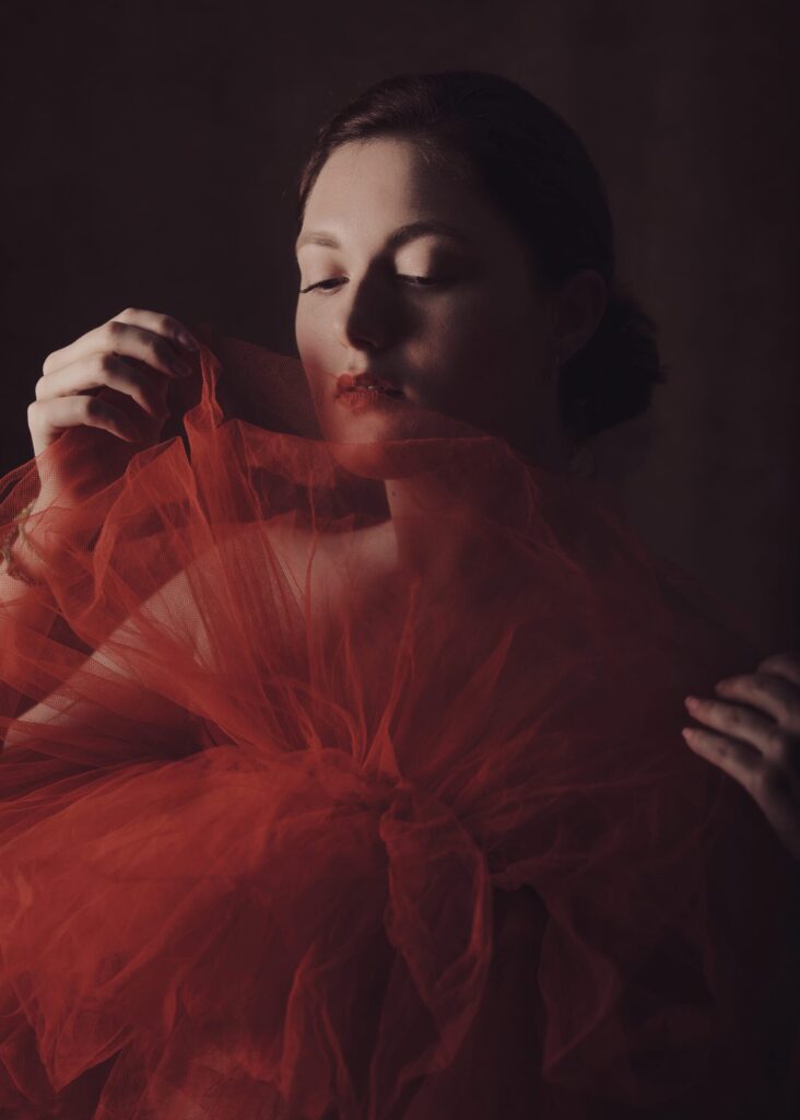 portrait de jeune femme en clair obscur effet vintage se cachant derrière un tulle rouge