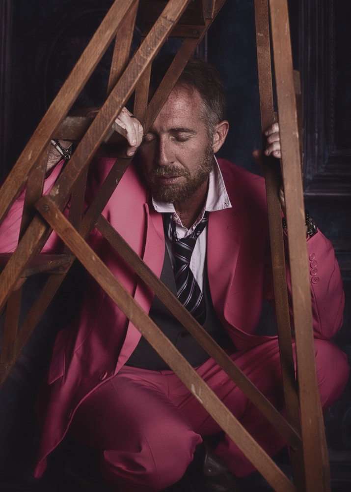 portrait d'un homme barbu en costume rose et cravate sous un escabeau ancien