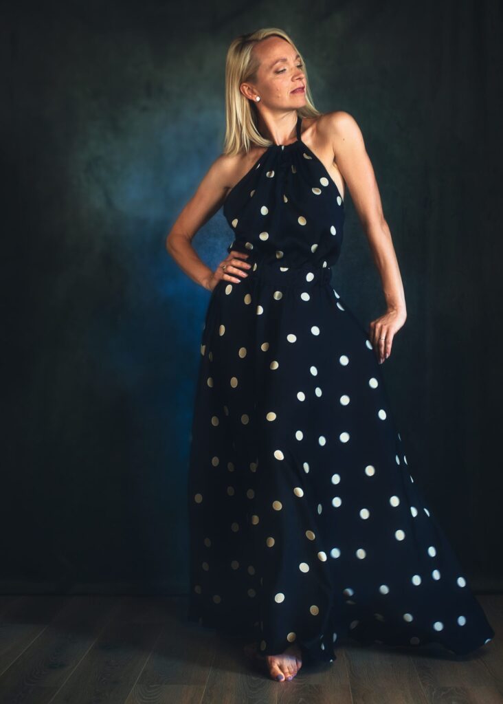 femme blonde élancée portant une robe à pois debout de face sur un fond bleu
