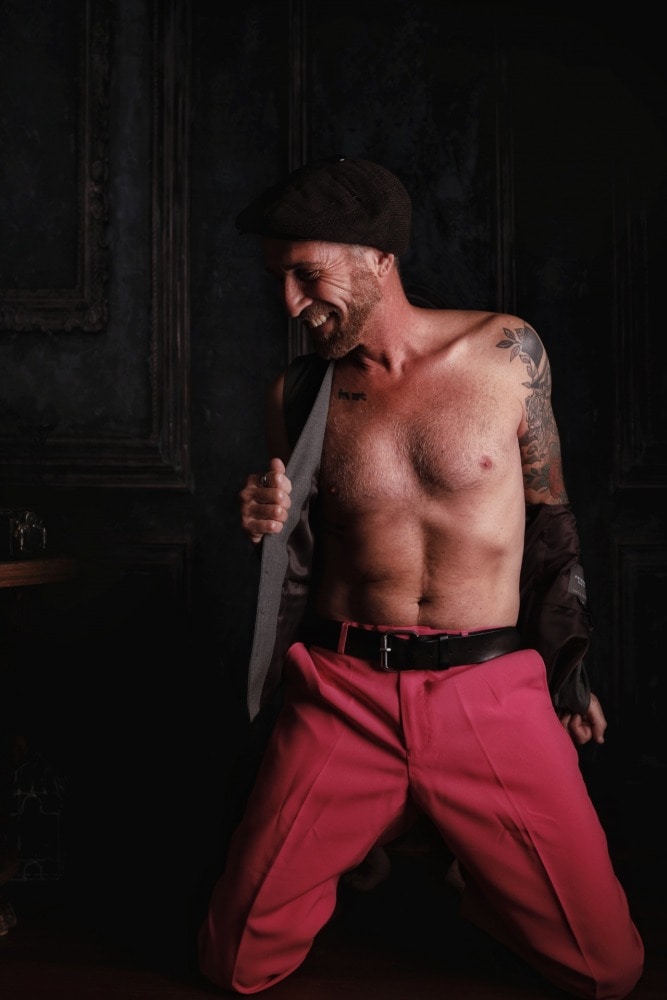 homme tatoué torse nu souriant dans un pantalon rose