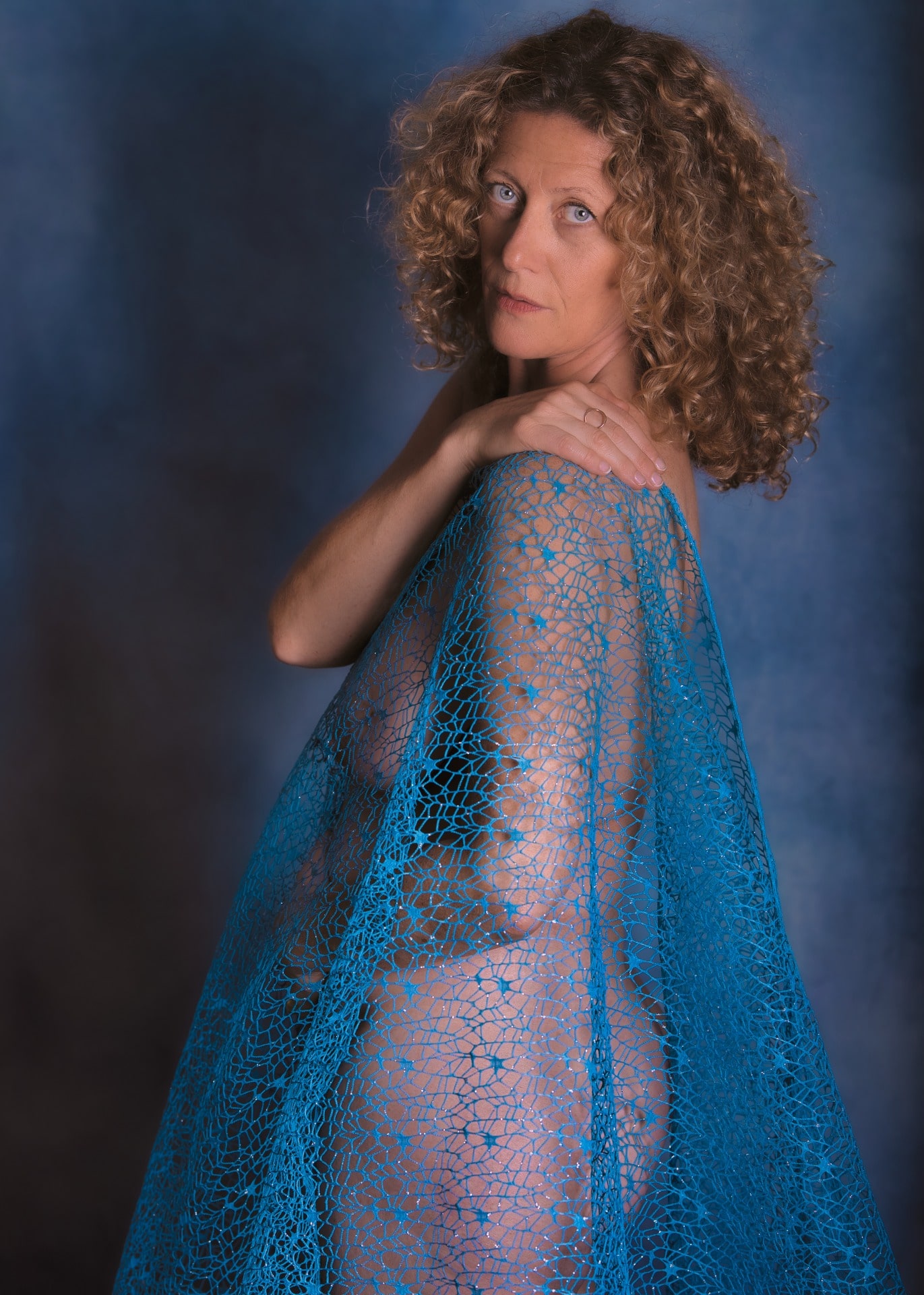 femme en nu artistique aux cheveux dorés bouclés yeux bleus sous un tissu bleu