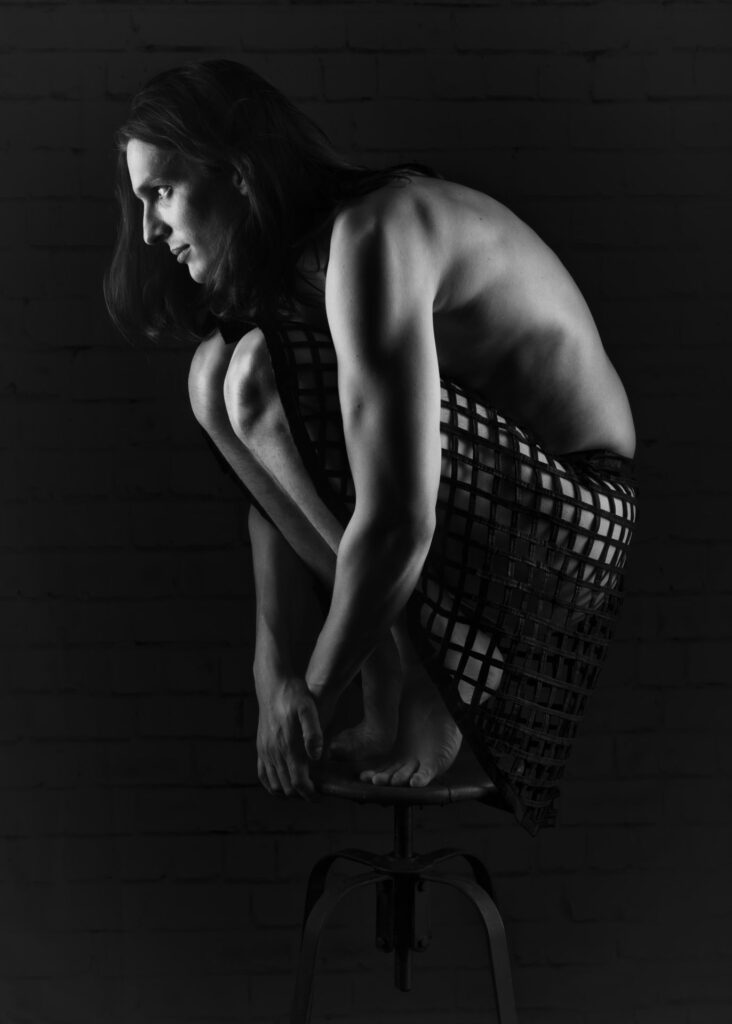 homme en nu artistique de profil accroupi sur un tabouret haut ancien en clair obscur portrait une jupe gothique noir et blanc