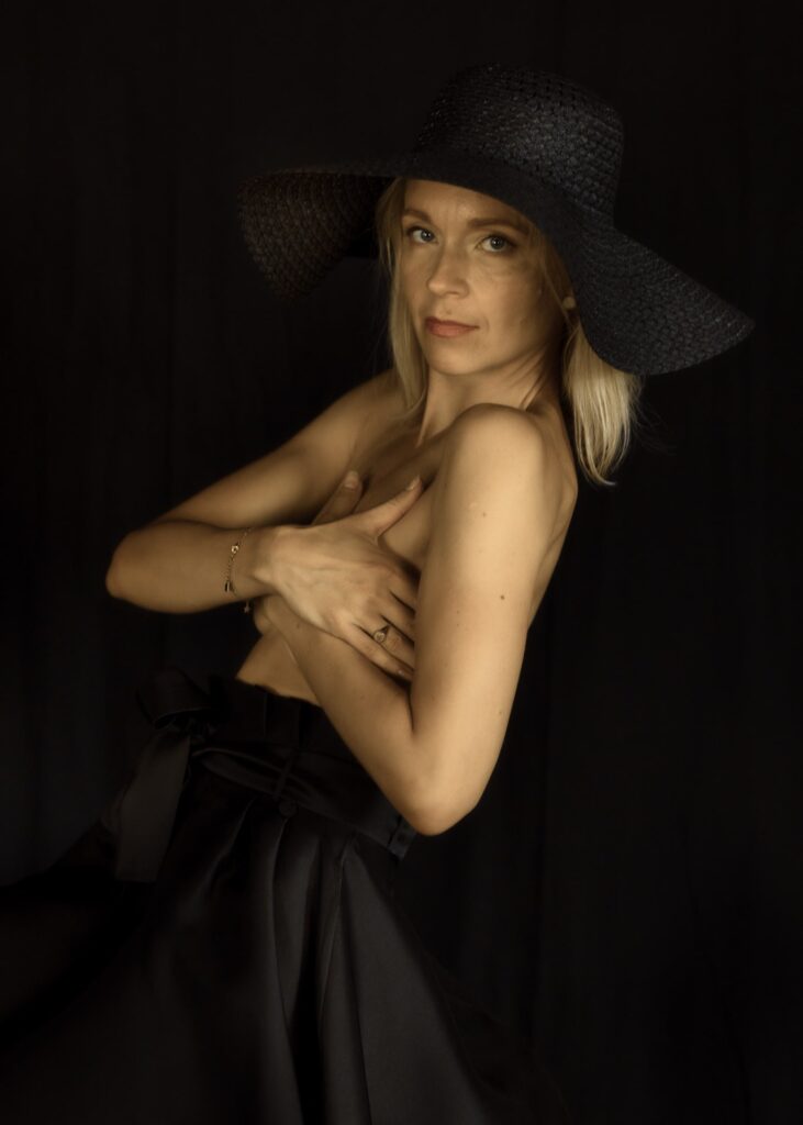 portrait d'une femme blonde de profil portant un chapeau noir et une robe noire