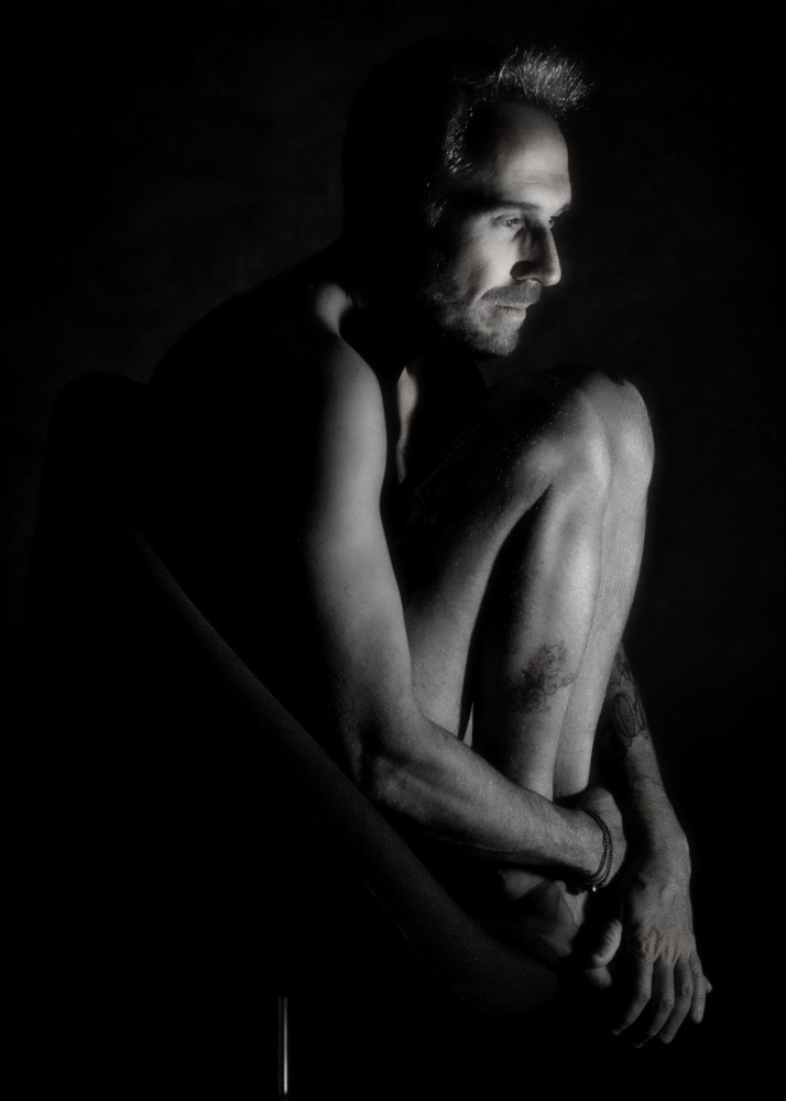 homme en nu artistique en boule dans un fauteuil en clair obscur 