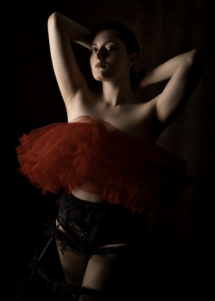 portrait d'une jeune femme habillé d'un tutu rouge et d'une crinoline noire les bras relevés derrière la tête