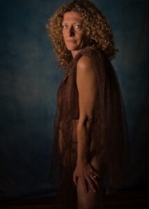 femme aux cheveux bouclés dorés en nu artistique de profil portant un tissu marron transparent en dentelles