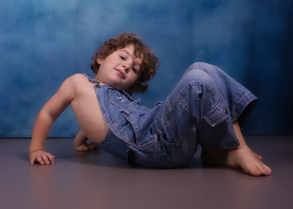 enfant petit garçon moins de 5 ans posant allongé sur le sol les jambes croisées en salopette jean