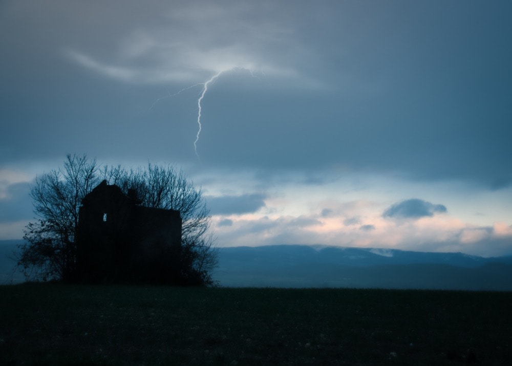 Une maison abandonnée envahie par un arbre en hiver dans la campagne sous l’orage