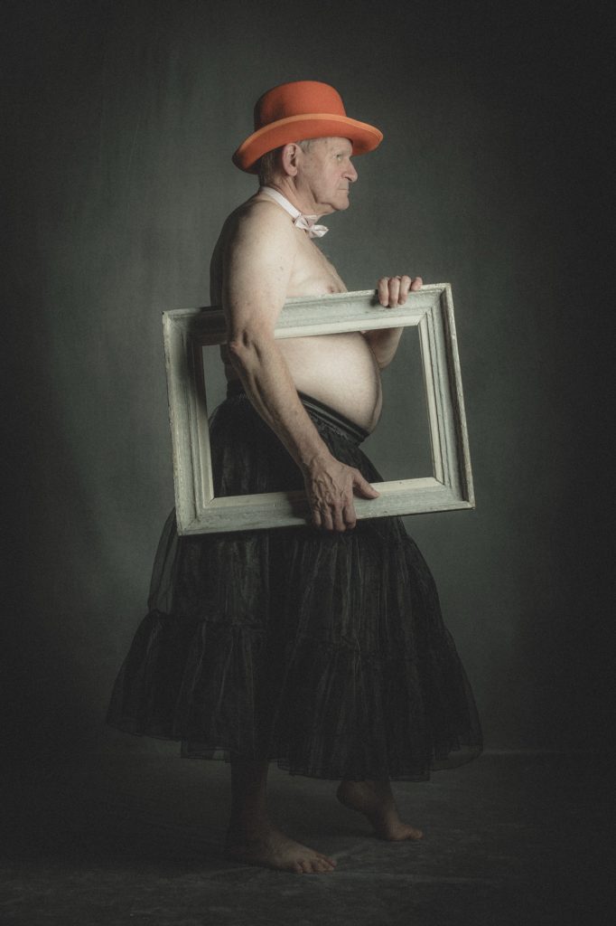 Séance photo shooting burlesque pour homme mature rond gros nu avec Mj-Nin modèle silver en jupon avec un cadre tableau vide et chapeau orange par Céline Pivoine Eyes femme photographe au studio photo location à Montreuil 93 près de Vincennes 