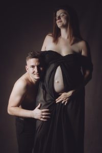 Séance couple enceinte estime avec Sarah et Benoît robe noire debout sourire sépia par femme photographe grossesse au studio photo location Céline Pivoine Eyes à Montreuil 93 près de Paris 