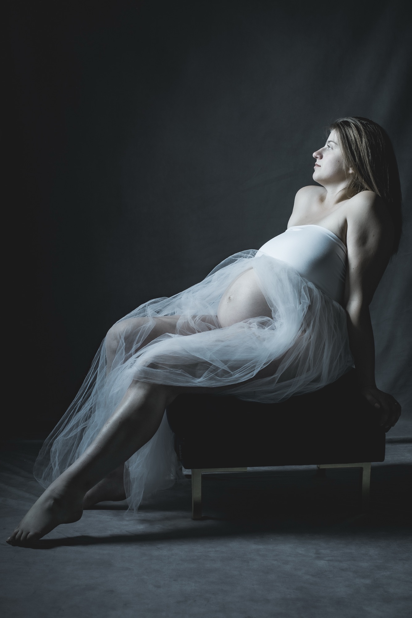Séance grossesse pour couple photographe famille enceinte avec Sarah en robe blanche tulle sur pouf par céline pivoine eyes femme photographe au studio photo location à Montreuil 93 près de Fontenay sous Bois