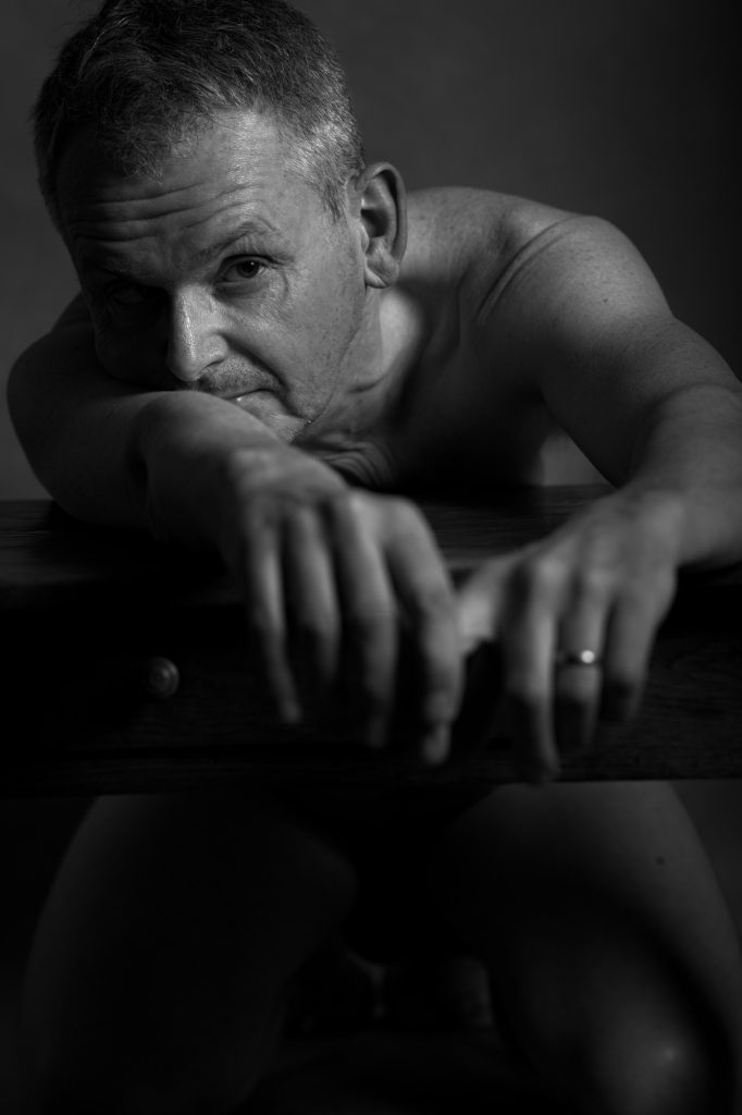 Séance photo estime de soi nu artistique pour homme mature sénior silver avec Jean-Yves en noir et blanc au studio photo de Céline Pivoine Eyes femme photographe à Montreuil 93 près de Vincennes portrait sur table regard