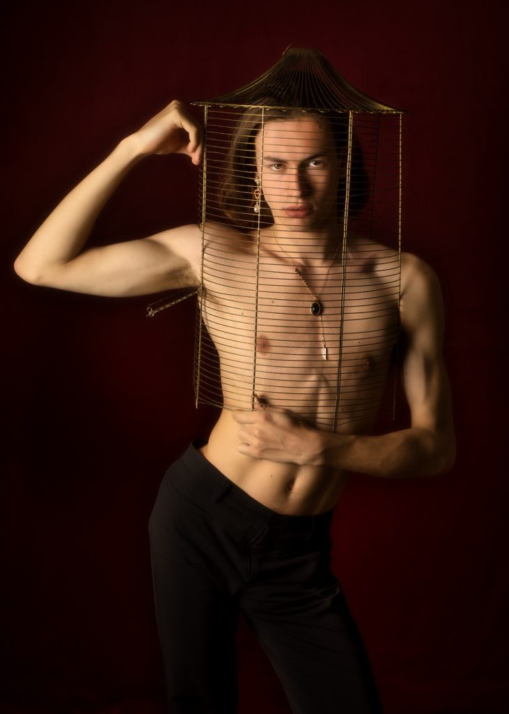 Séance photo shooting pour modèle homme androgyne les féminins par femme photographe céline pivoine eyes au studio photo location à Montreuil 93 près de Vincennes torse nu dans un cage portrait fond rouge