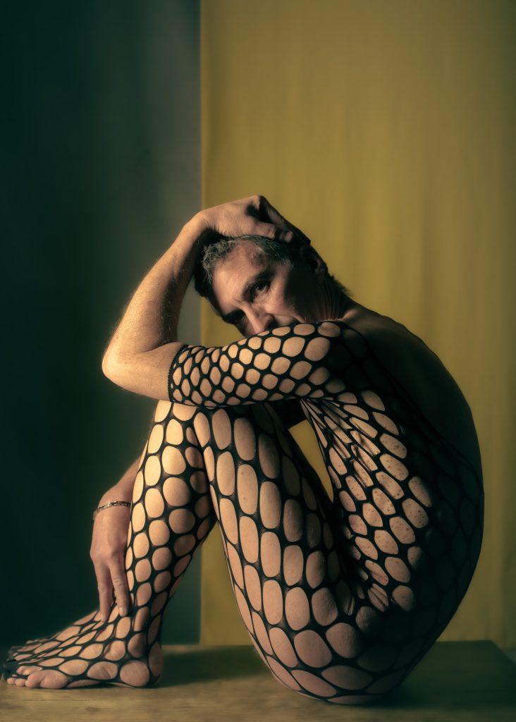 séance photo shooting pour modèle vivant homme nu avec Marco par femme photographe céline pivoine eyes au studio photo location à Montreuil 93 près de Vincennes en combinaison résilles sur fond jaune assis de profil les féminins