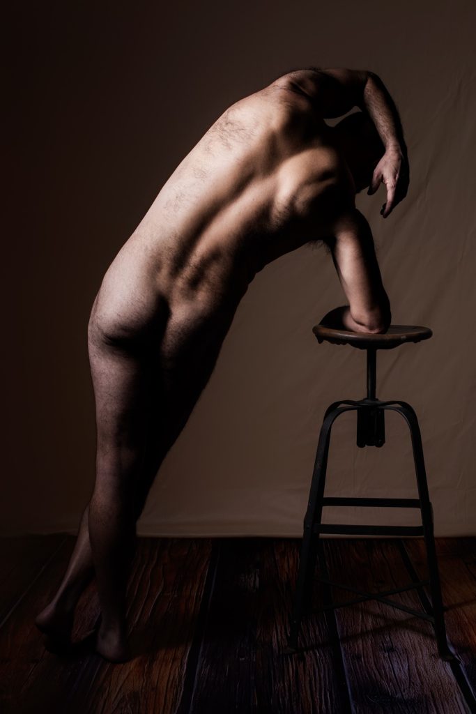 Séance photo shooting boudoir pour homme nu avec Philippe musclé sportif de dos debout penché sur un tabouret 