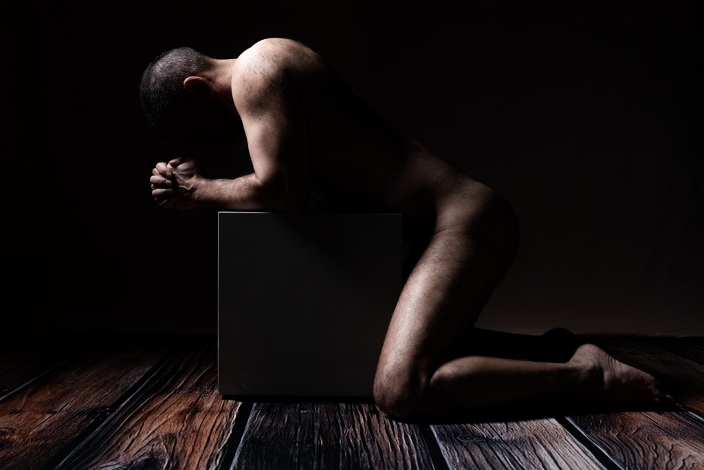 Séance photo shooting boudoir pour homme nu avec Philippe musclé sportif de profil à genoux devant un cube clair obscur 