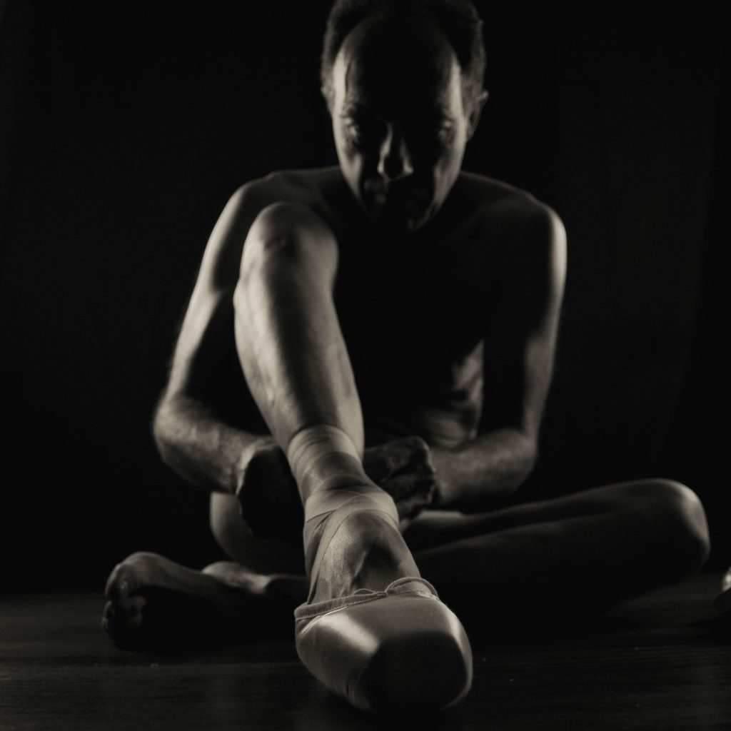 Séance shooting photo pour homme mature nu danseur yoga souplesse clair obscur noir et blanc assis de face au sol avec chaussons pointes