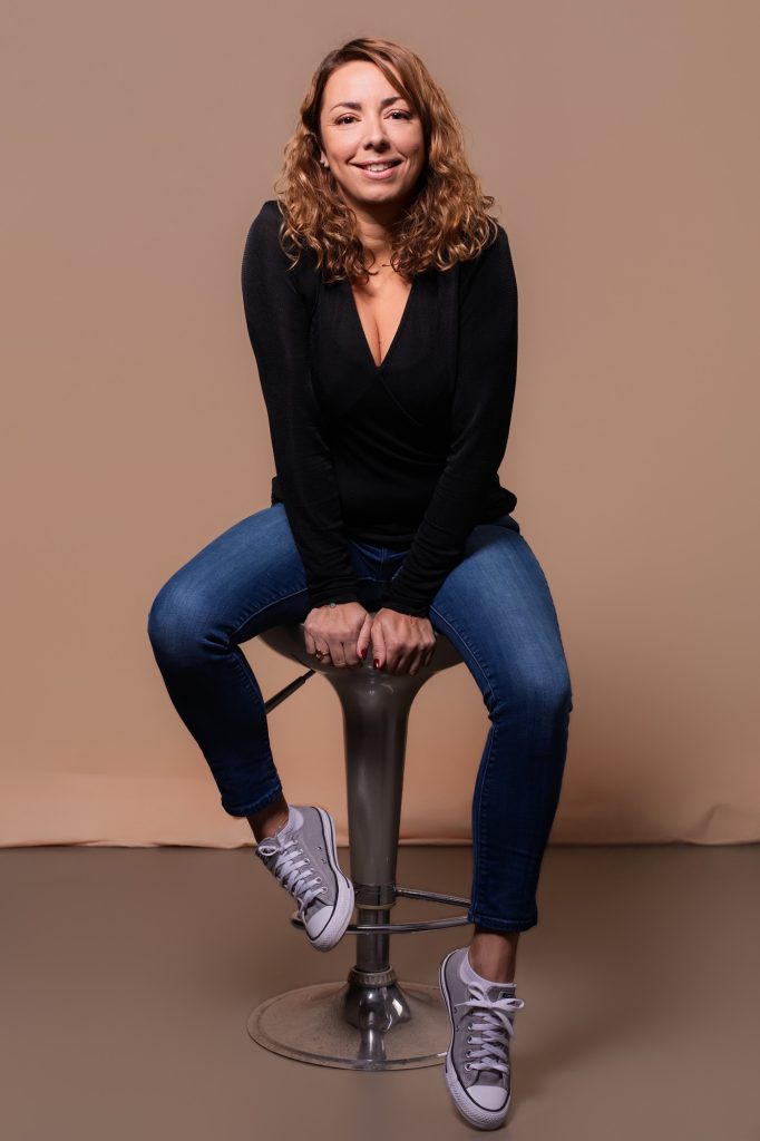 Séance portrait estime de soi avec Vanessa Bois souriante assise sur un tabouret en jean et pull noir basket