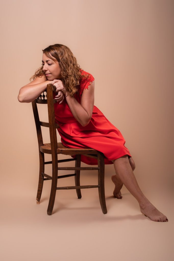 Séance portrait estime de soi avec Vanessa pensive assise sur une chaise ancienne en bois en robe corail pied nu