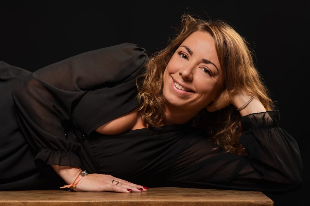 Séance portrait estime de soi avec Vanessa souriante en robe noire de profil allongée sur une table