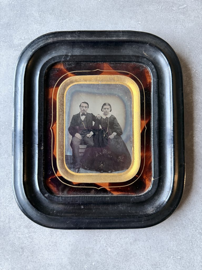 Ambrotype sous cadre laqué façon écaille et passe-partout doré : portrait d'un couple assis, l'homme barbu en costume sombre, la femme en robe à crinoline, bijoux rehaussés à l'or, vers 1858-1865.