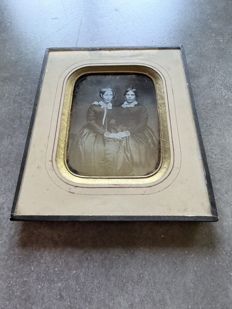 Daguerréotype sous verre : double portrait de deux jeunes femmes assises côte à côte, robes sombres et cols de dentelle, se ressemblant fortement, vers 1850-1855.