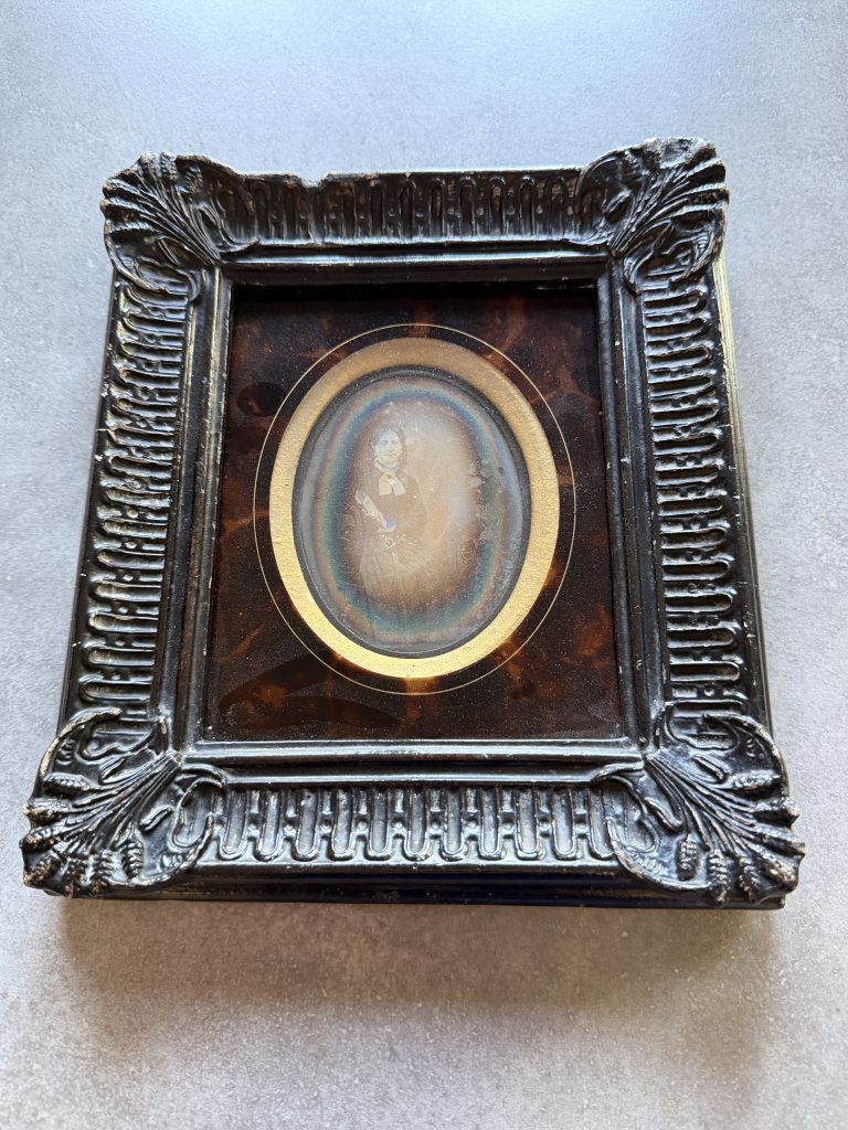 Daguerréotype dans un cadre noir mouluré de style Napoléon III : portrait de buste, en médaillon ovale, d'une femme au bonnet de jour clair et robe sombre, vers 1845-1855.