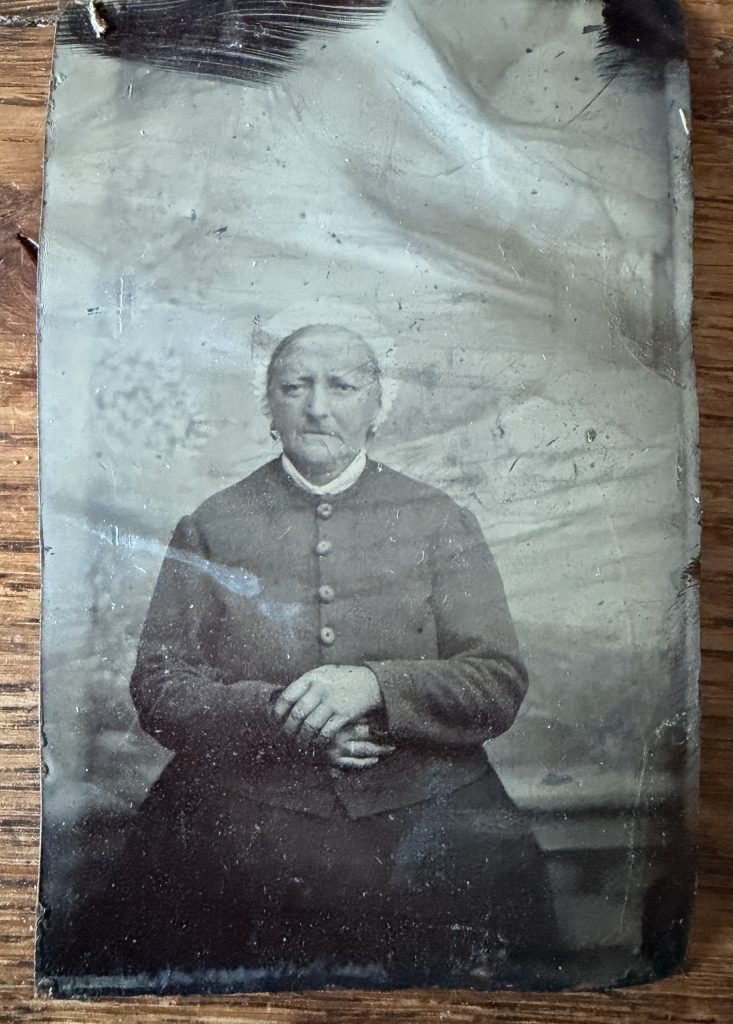 Ferrotype (tintype) sur plaque de fer verni noir, sans monture : portrait assis d'une femme âgée en coiffe blanche et col de dentelle, mains jointes, vers 1875-1900.
